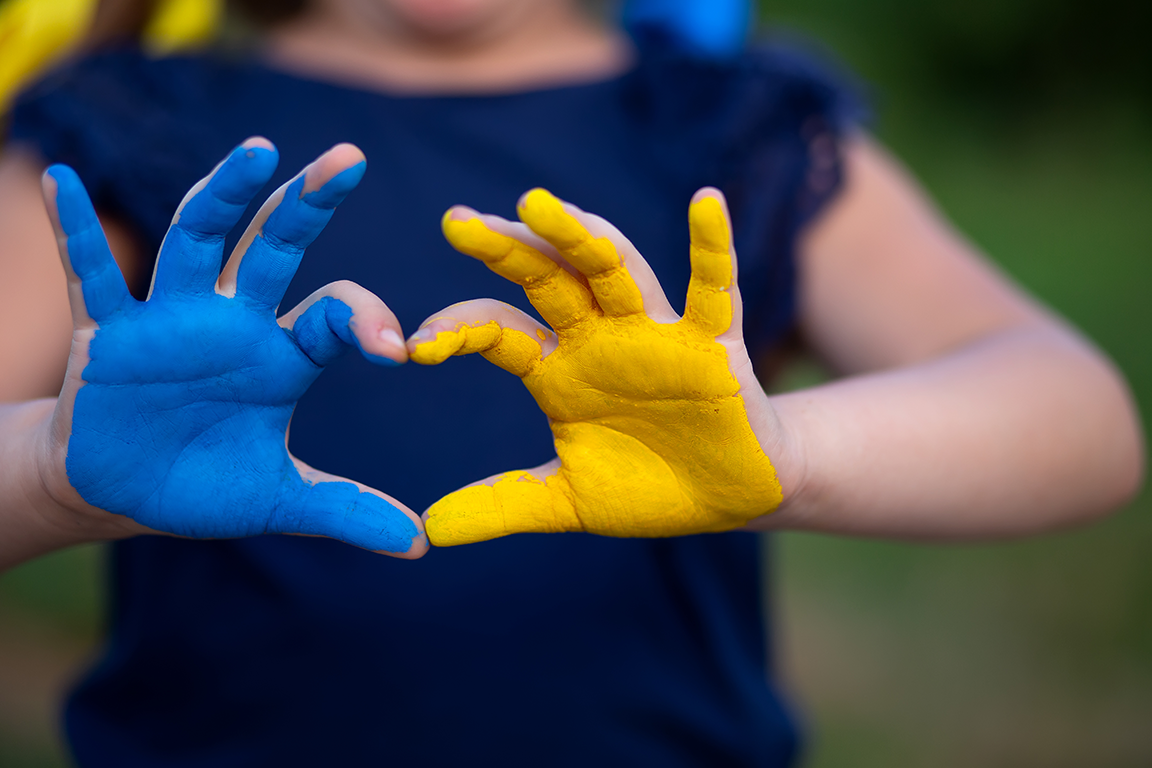 A child forms a heart with hands painted the colors of the Ukrainian flag.